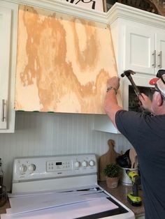 a man working on a kitchen cabinet with tools in his hand and an unfinished piece of wood hanging above the stove