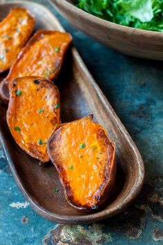 baked sweet potato wedges on a wooden spoon with lettuce in the background