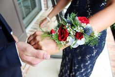 two people in formal wear holding hands with flowers on their wrist and one person wearing a suit