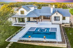 an aerial view of a house with a swimming pool in the foreground and landscaping around it