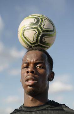 a man balancing a soccer ball on his head in front of a cloudy blue sky