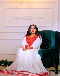 a woman sitting in a green chair wearing a white and red outfit with gold accents