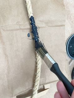 a hand holding a paintbrush next to a piece of rope