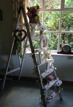 a ladder decorated with flowers and letters in front of a window, next to a clock