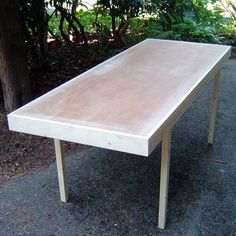 a wooden table sitting on the side of a road next to a tree and bushes