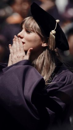 a woman wearing a graduation gown and holding her hands up to her face while standing in front of an audience