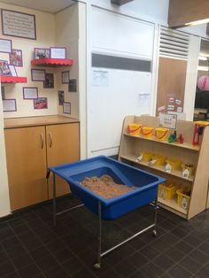 a blue wheelbarrow filled with sand in front of a desk and shelves on the wall