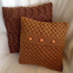 two brown knitted pillows sitting on top of a white bed next to each other