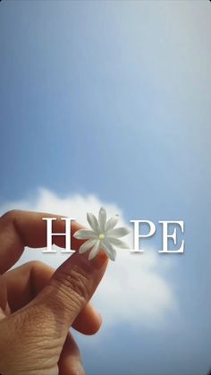 a hand holding a small flower with the word hope in it's center against a blue sky