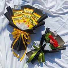 two bouquets of flowers are wrapped in black paper and tied with yellow ribbon on a white sheet