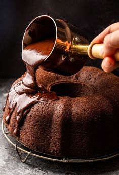 someone pouring chocolate sauce on top of a bundt cake