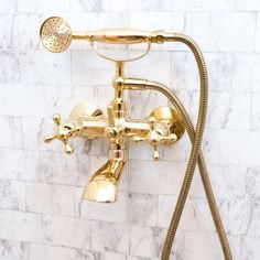 a gold faucet shower head and hand shower in a white tiled bathroom with marble walls