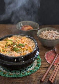 a bowl of soup with chopsticks and rice on a table next to it