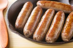 several sausages in a frying pan next to a wooden spoon