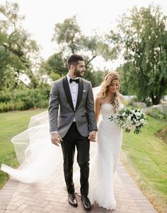 a bride and groom walking down a path holding hands