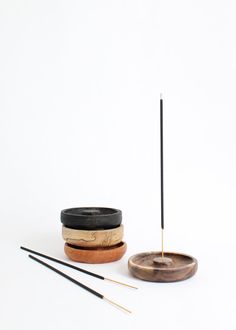 two wooden bowls with sticks in them on a white surface next to a small black and gold incense stick