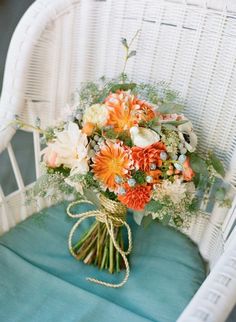 a bridal bouquet sitting on top of a white chair next to a blue pillow