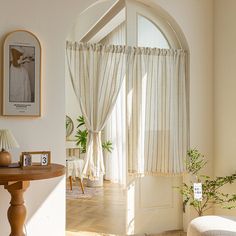 a living room with an arched window and white curtains on the windowsill, next to a small table with a potted plant