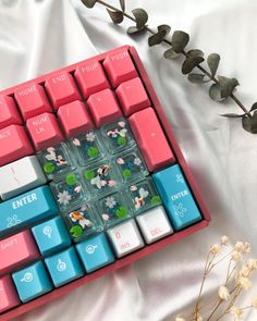 a pink and blue keyboard sitting on top of a white sheet next to flowers with leaves