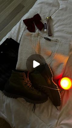 a pair of boots, sweaters and other items are on a bed with a candle