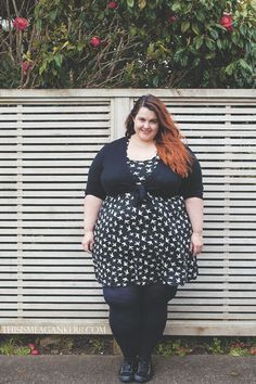 a woman standing in front of a white fence with flowers on it and wearing black tights