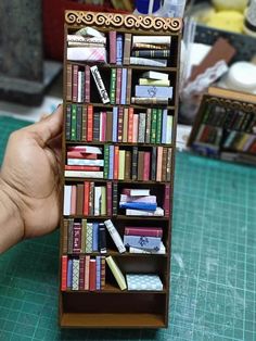 a hand holding a miniature book shelf filled with books