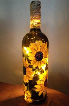 a glass bottle with sunflowers on it is sitting on a table next to a lamp