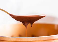 a spoon full of melted chocolate sitting on top of a wooden bowl filled with liquid