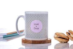 two donuts are next to a coffee mug on a wooden stand with the words bis mil lah printed on it