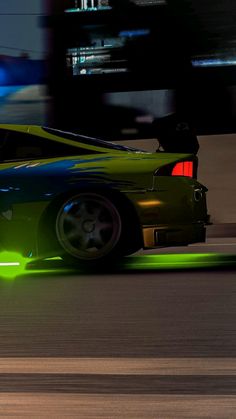 a green sports car driving down the road at night time with its hood up and tail lights on