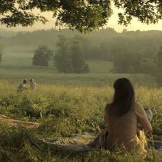 a woman sitting on top of a blanket in a field next to trees and people