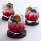 three glasses filled with fruit and ice on top of a white table next to each other