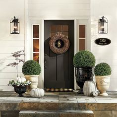 front porch decorated for fall with pumpkins and potted topiaries on steps