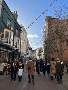 many people are walking down the street in front of shops and buildings on a sunny day