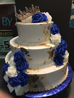 a three tiered cake with blue and white flowers on the bottom, topped with a crown