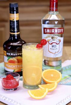 an alcoholic drink with oranges and vodka on a tray next to it's bottles