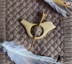 two feathers and a wooden brooch sitting on top of a piece of fabric next to a feather quill