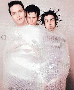 three young men wrapped in plastic wrap posing for the camera with their hair flying through the air