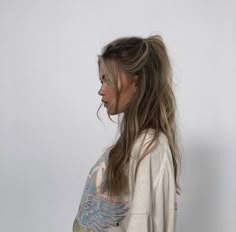 a woman with long hair standing in front of a white wall and looking off to the side