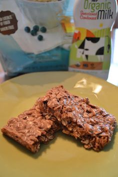 two granola bars on a yellow plate next to a bag of milk and cereal