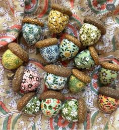 many different types of painted eggs on a table cloth with pine cones and leaves around them