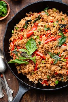 a skillet filled with rice and vegetables on top of a wooden table next to silverware