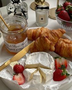 cheese, strawberries and croissants on a plate with a jar of honey