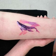 a woman's arm with a pink and purple whale tattoo on it