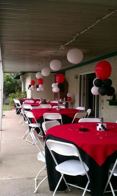 red, black and white balloons are hanging from the ceiling above tables at a party