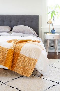 a bed with a blanket on top of it next to a night stand and table