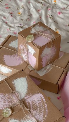 three brown boxes with pink and white designs on them sitting on a floral bed sheet