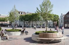 people are sitting on benches in the middle of a courtyard with trees and buildings behind them