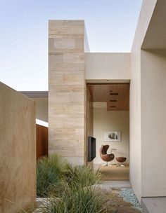 an entrance to a modern home with plants in the foreground and a chair on the far side