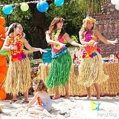 three women in hula skirts are dancing on the beach with balloons and streamers